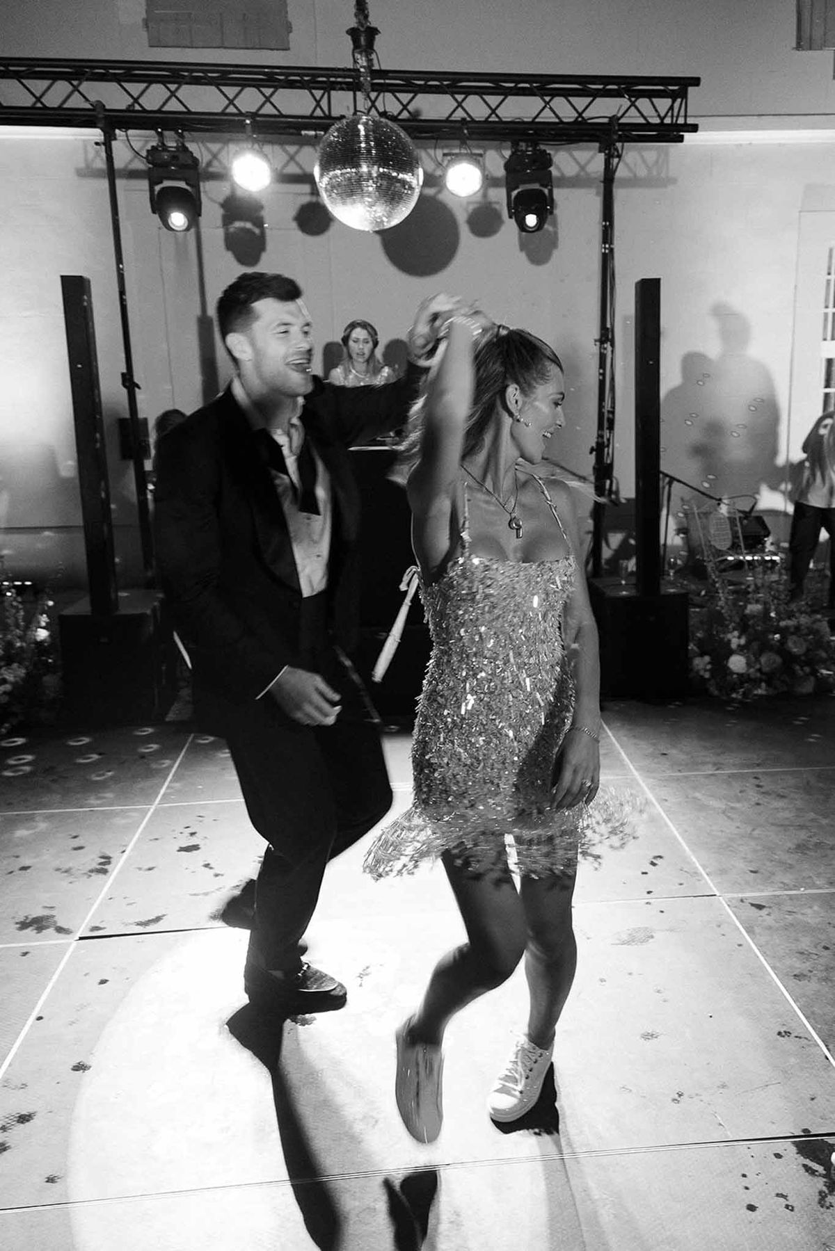 Black and white photo of couple dancing under disco ball during wedding after-party with fringed mini dress and sneakers