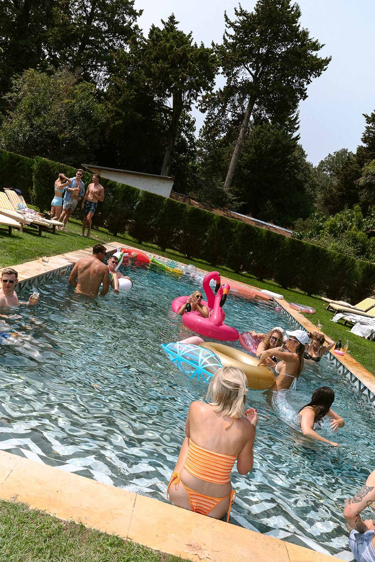 Guests enjoying pool party with colorful inflatables and champagne at private estate