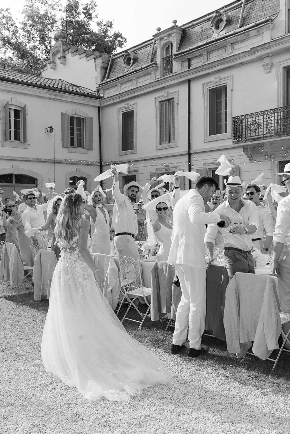 Couple enters between tables as 30 guests wave napkins and white hats in French tradition in B&W