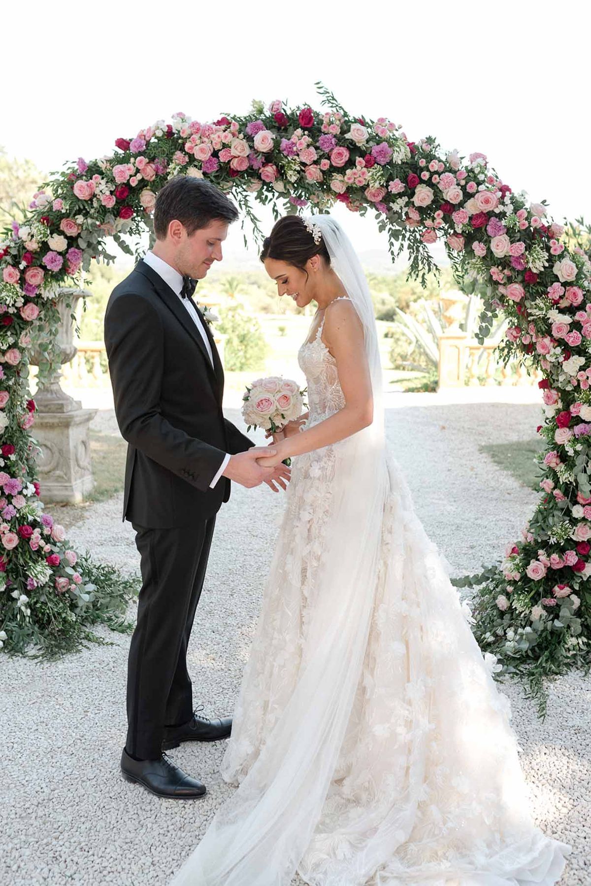 Couple beneath circular arch of blush hot pink and magenta roses with textured applique ballgown