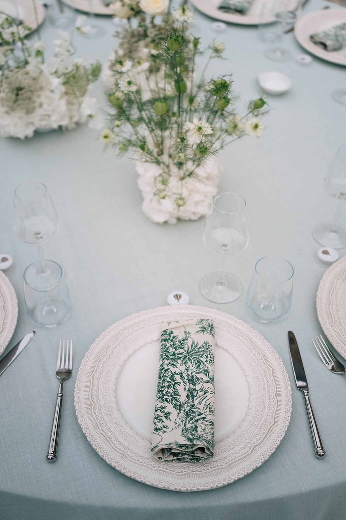 Reception place setting with scalloped charger plate, toile de Jouy napkin, and white floral centerpiece
