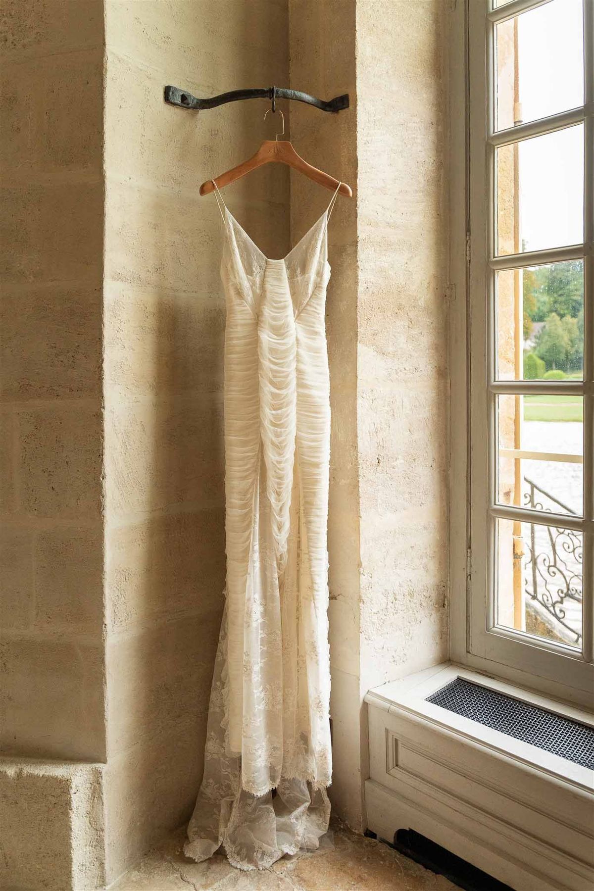 Lace wedding dress hanging in limestone alcove at Chateau de Villette