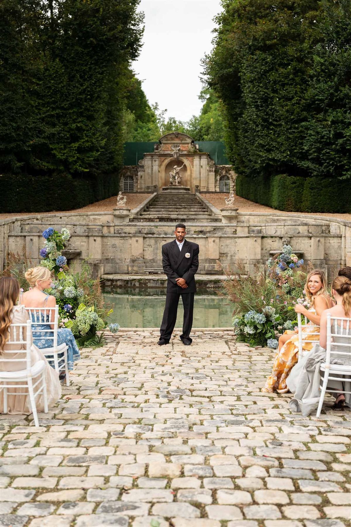 Groom waiting at ceremony aisle by cascade fountain at Chateau de Villette