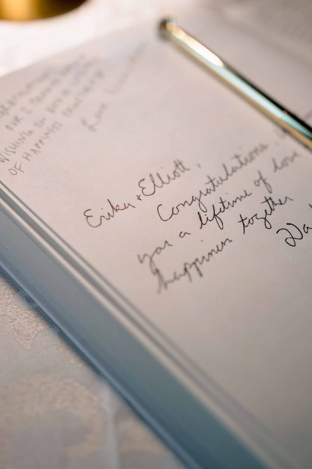 Open wedding guest book with handwritten message and silver pen on white linen surface