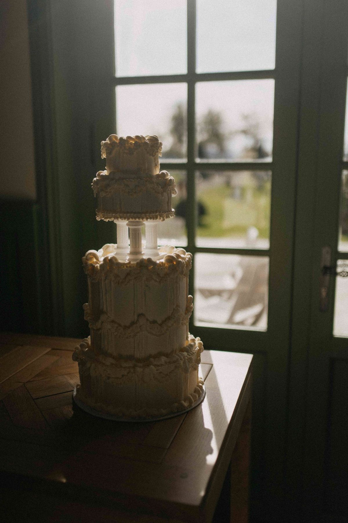 Tiered white cake with vintage piping backlit by a green paned door at golden hour