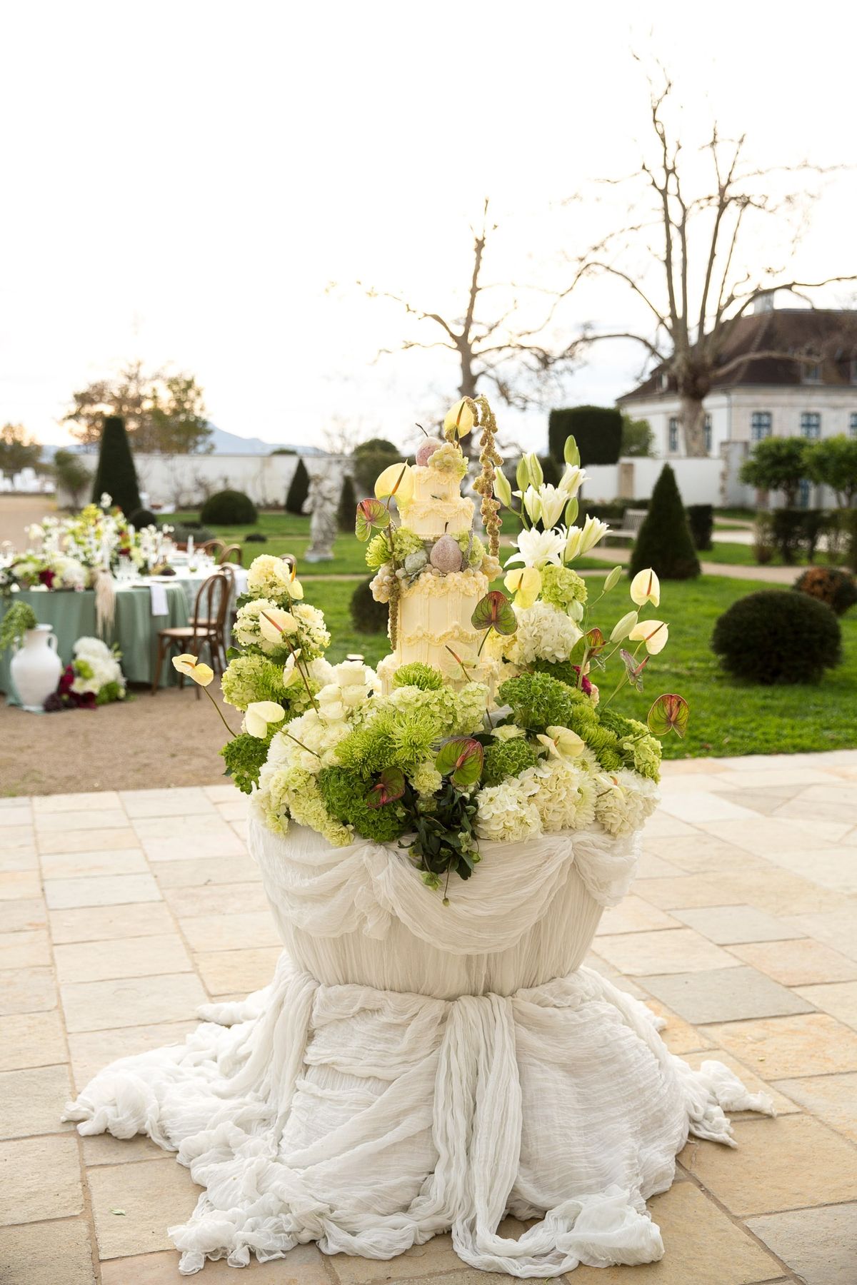 Garden cake plinth wrapped in white drape with cascading green and white florals around a tiered cake