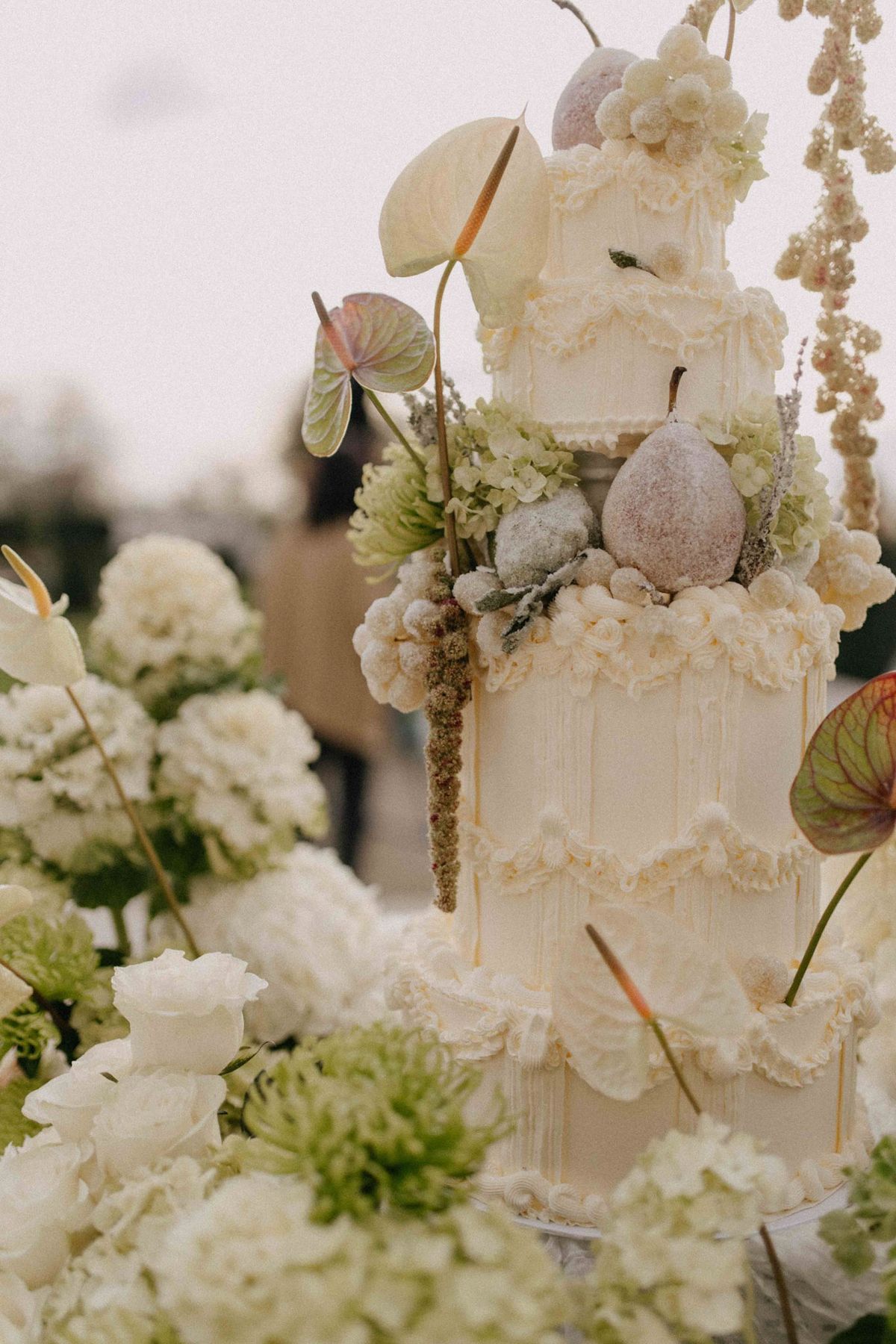 Tiered ivory cake close up with vintage piping, sugared pears and anthurium leaves