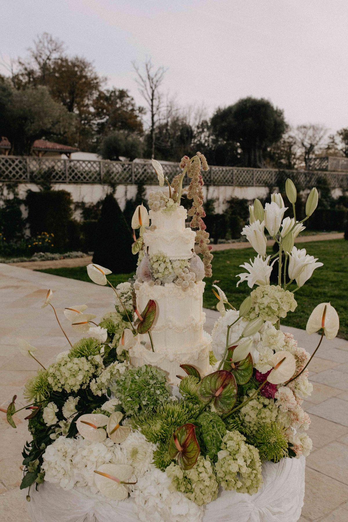 Tiered piped cake among green hydrangeas, lilies and anthuriums in the chateau garden