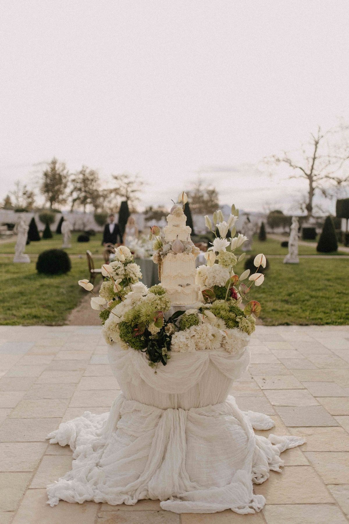 Floral cake plinth on the chateau forecourt with long reception table behind at twilight