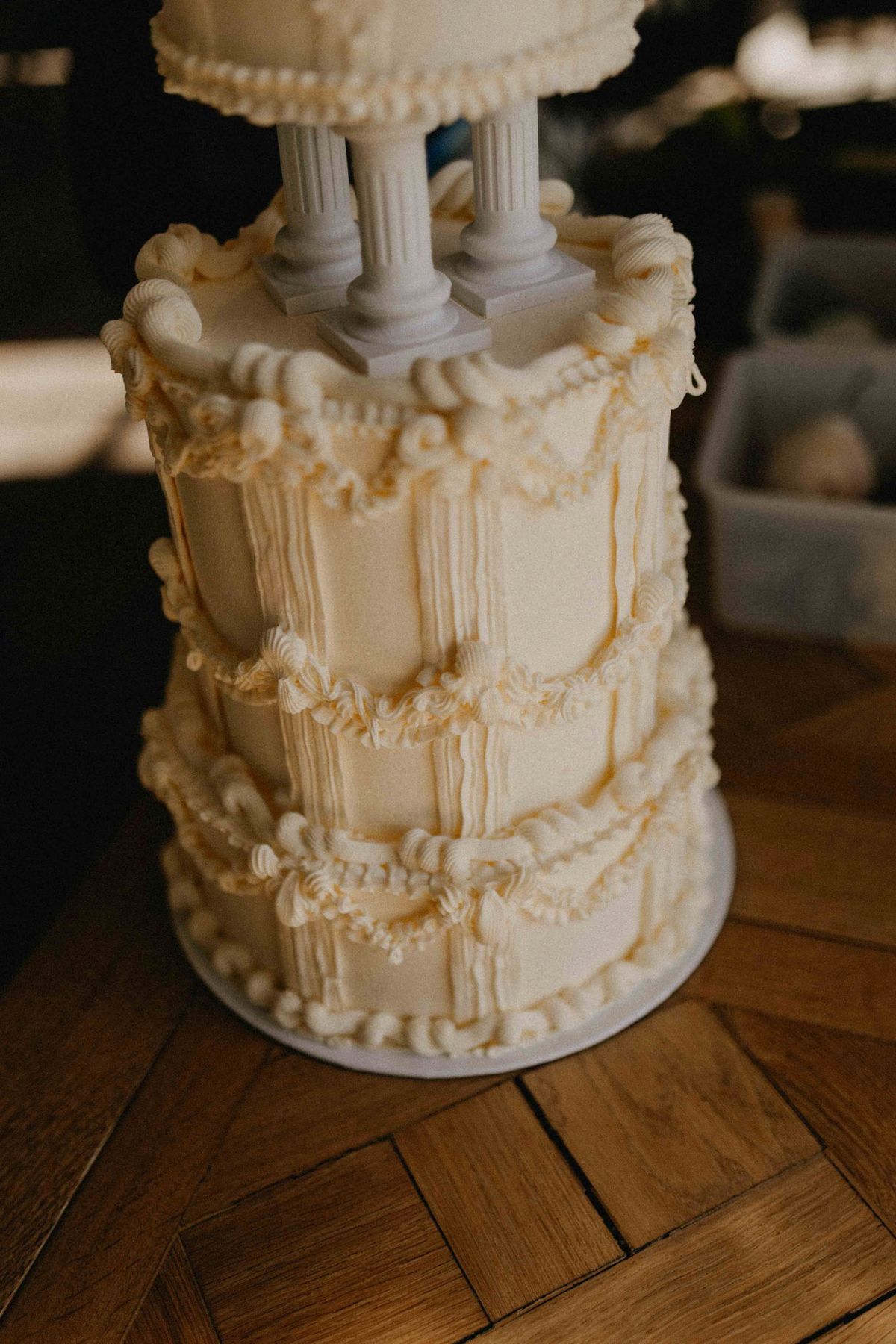 Ivory piped cake on grass beside a tipped ceramic vessel spilling white tassel detail