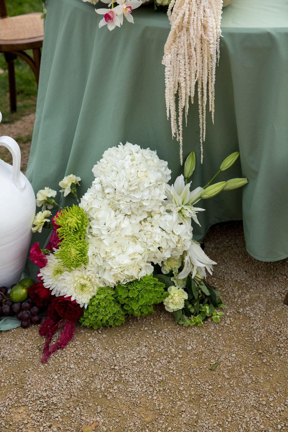 Floor level detail of white hydrangea and green chrysanthemum arrangement beside a sage draped table