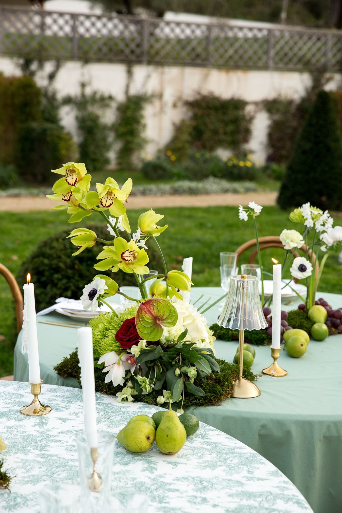 Garden tablescape with green orchids, anemones, taper candles, pears and grapes on moss runner