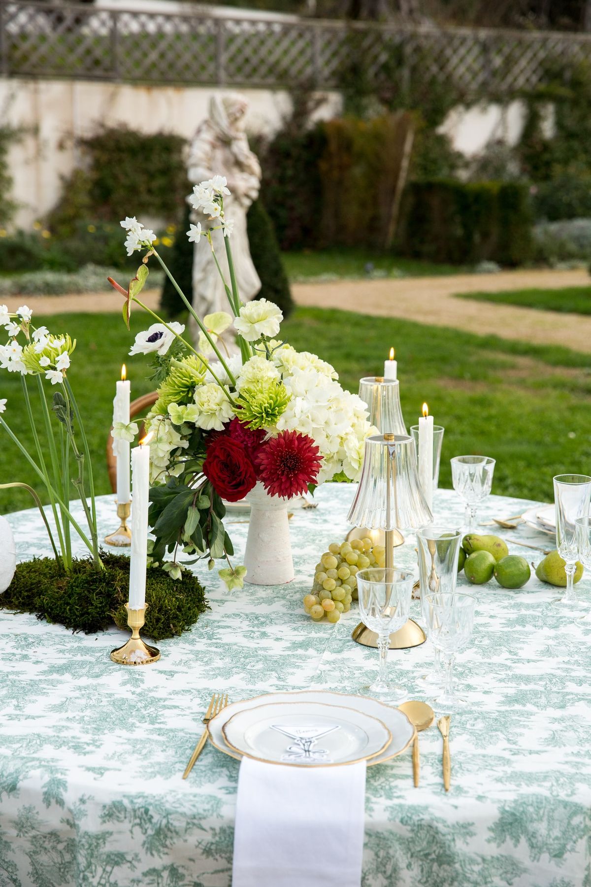 Garden tablescape with anemones, burgundy florals, brass candleholders and crystal goblets