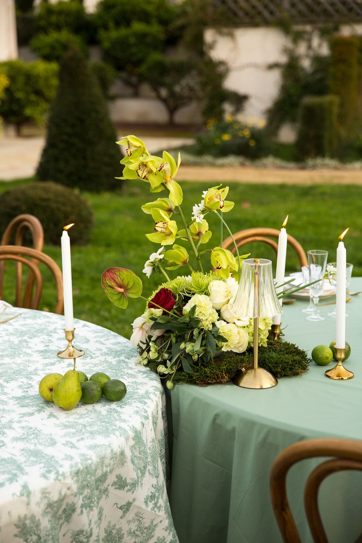 Side angle of moss runner, anthurium and orchids cascading off a sage cloth with limes and pear
