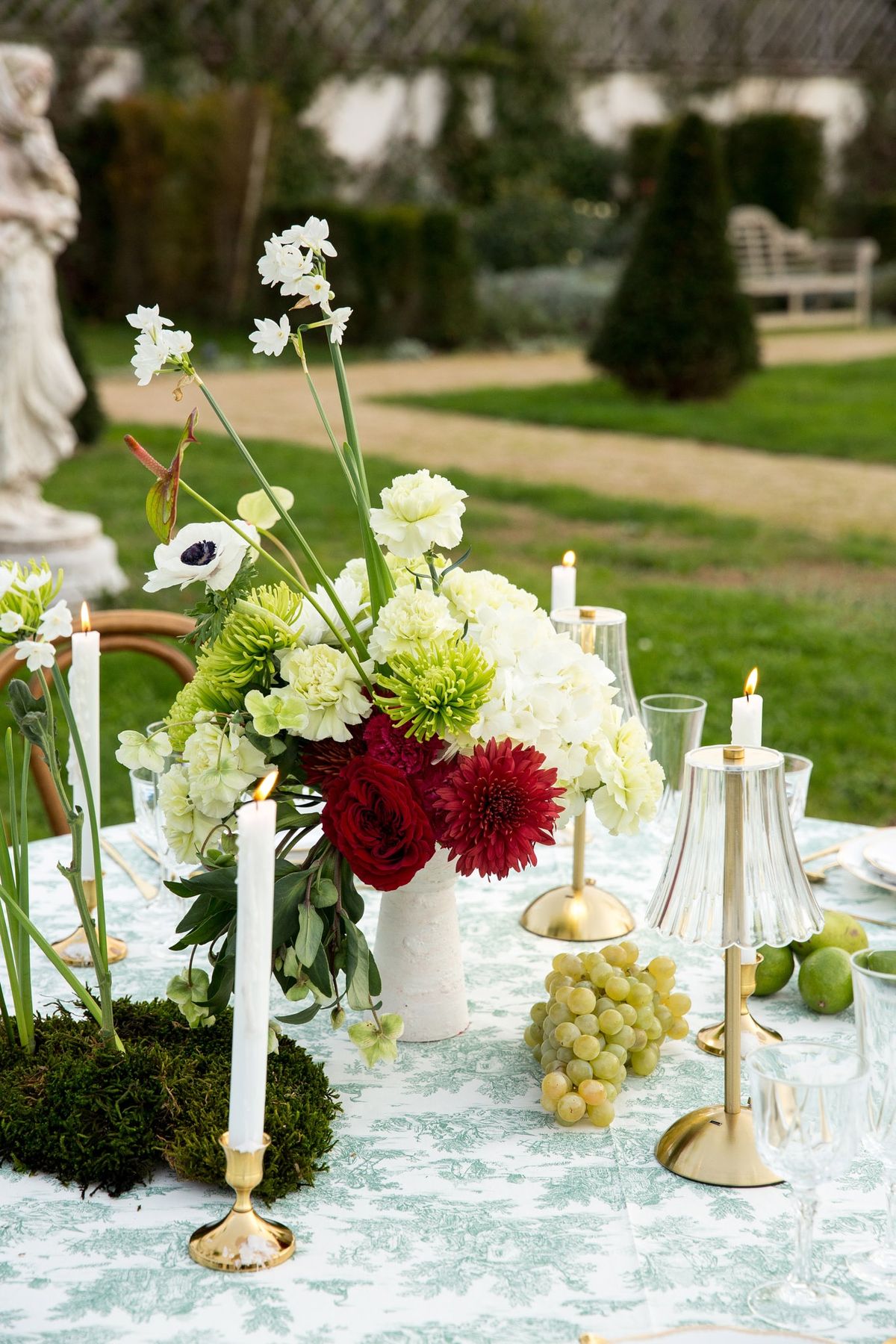 White urn with chrysanthemums, narcissus and burgundy dahlias on toile cloth with brass tapers