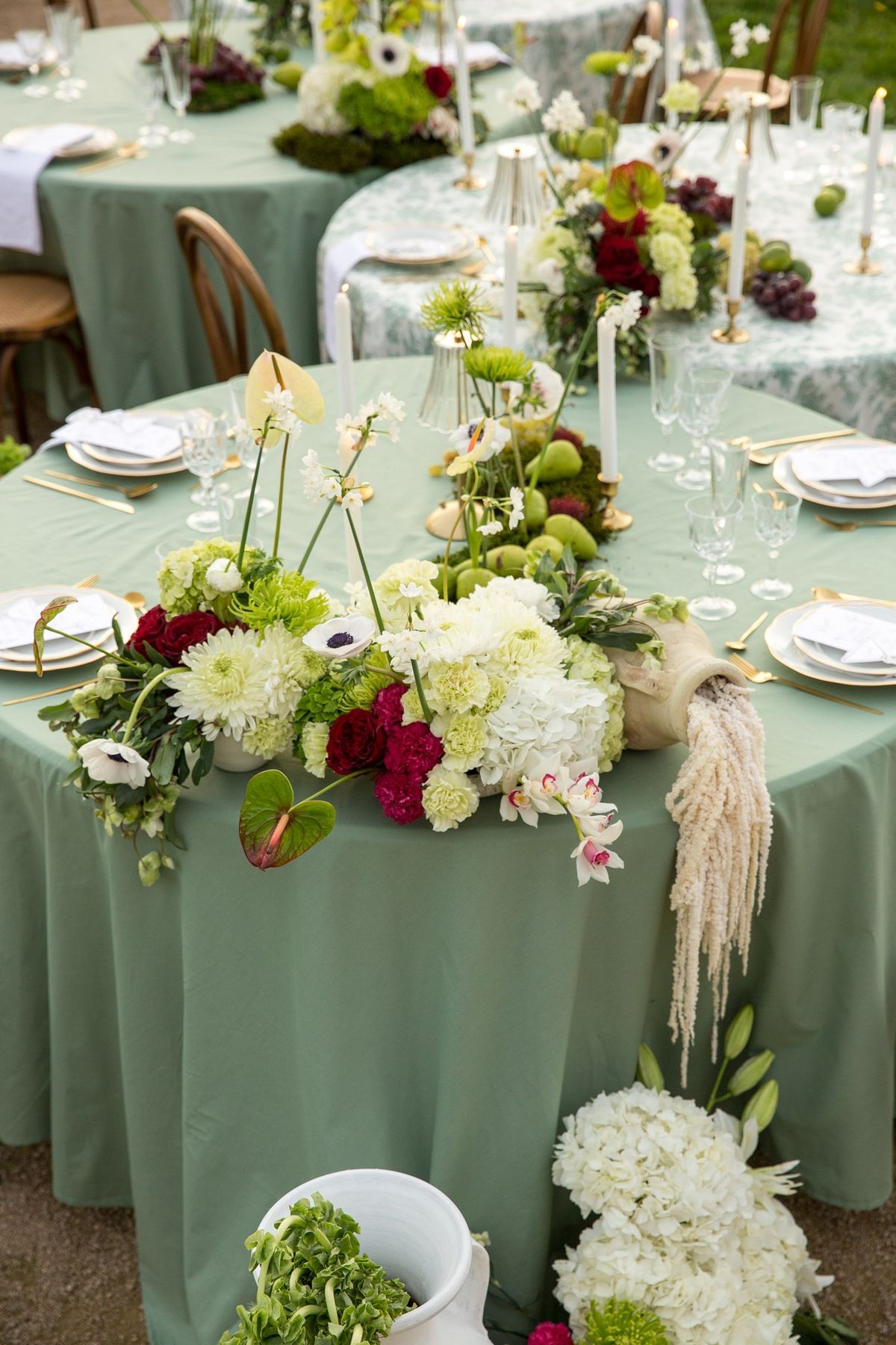 Two round sage tables from above with cascading floral centerpieces and amaranthus draping the edge