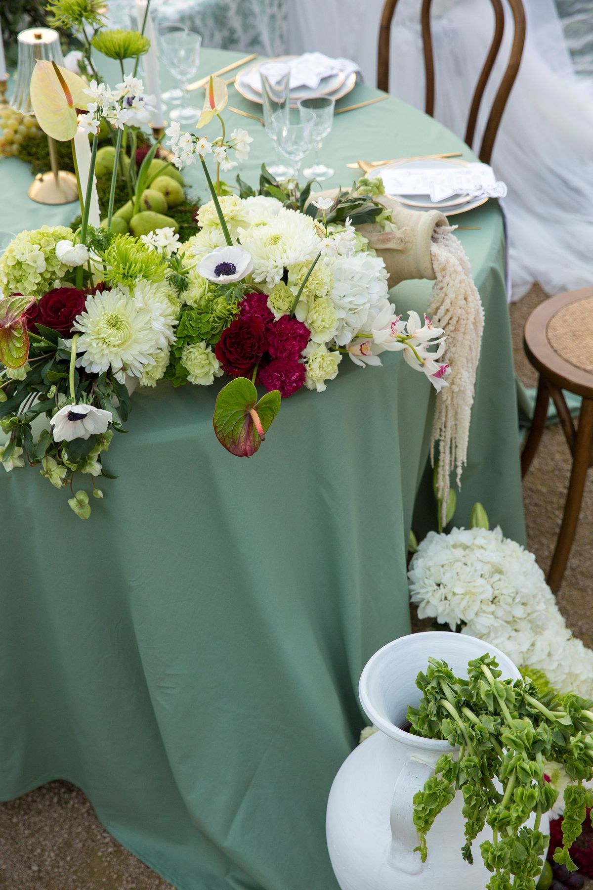 Cascading hydrangea and anthurium centerpiece spilling off a sage cloth, white pitcher below