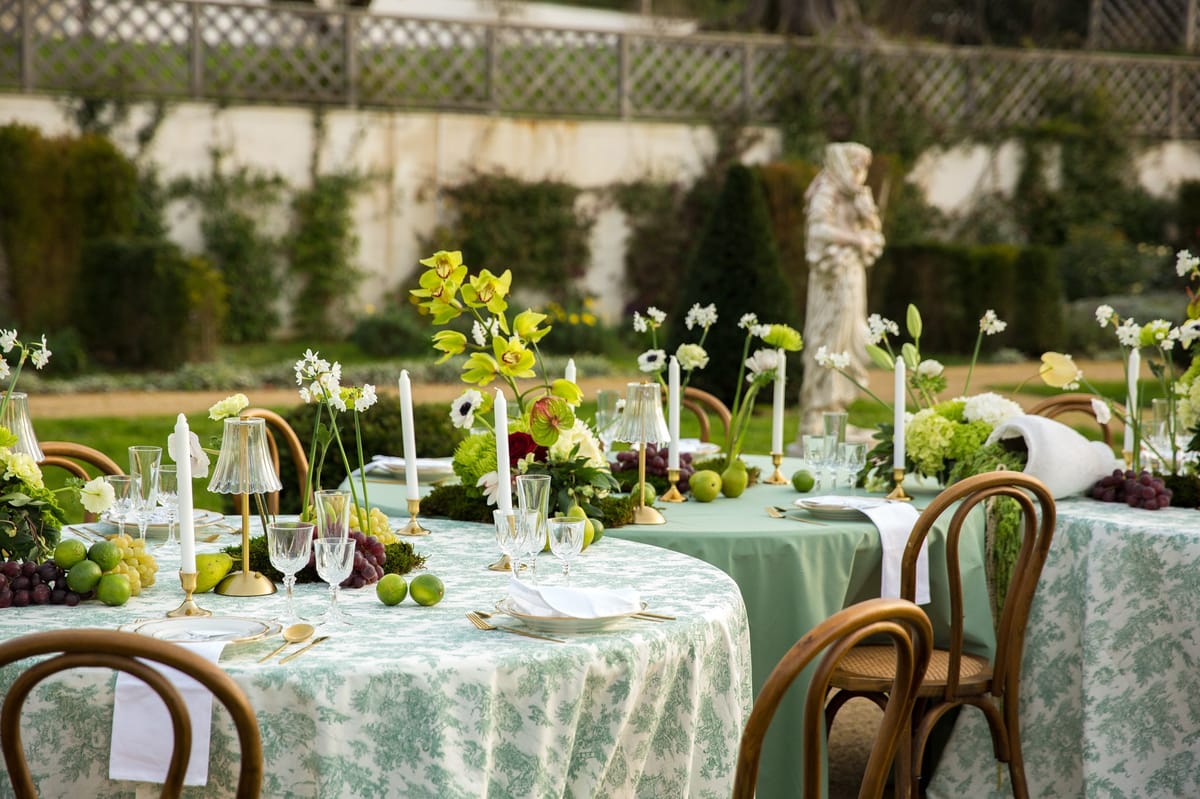 Sage cloth garden table backed by stone statue and clipped hedges with florals and amaranthus