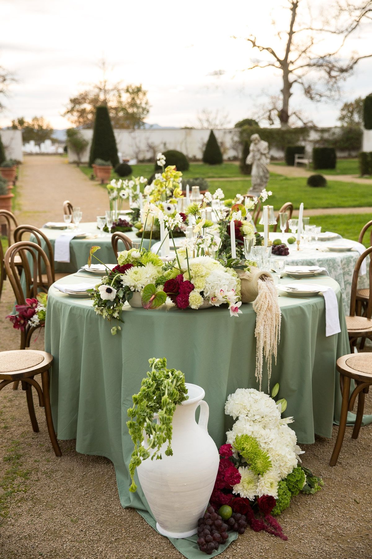 Sage table edge with cascading florals and amaranthus dripping to gravel, bench and topiary behind