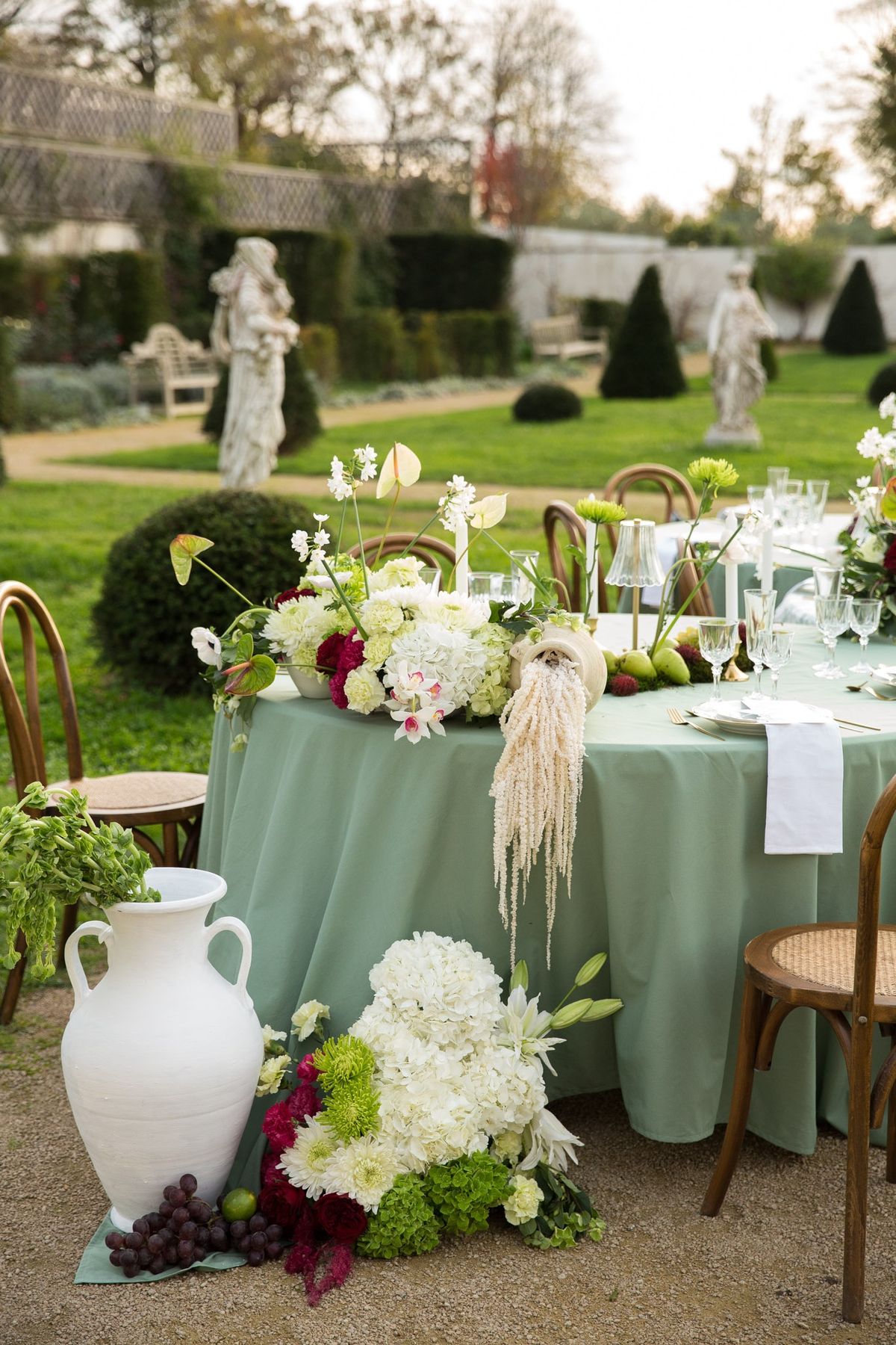 Twilight sage tablescape with stone statue centered in parterre and topiary cones bordering lawn