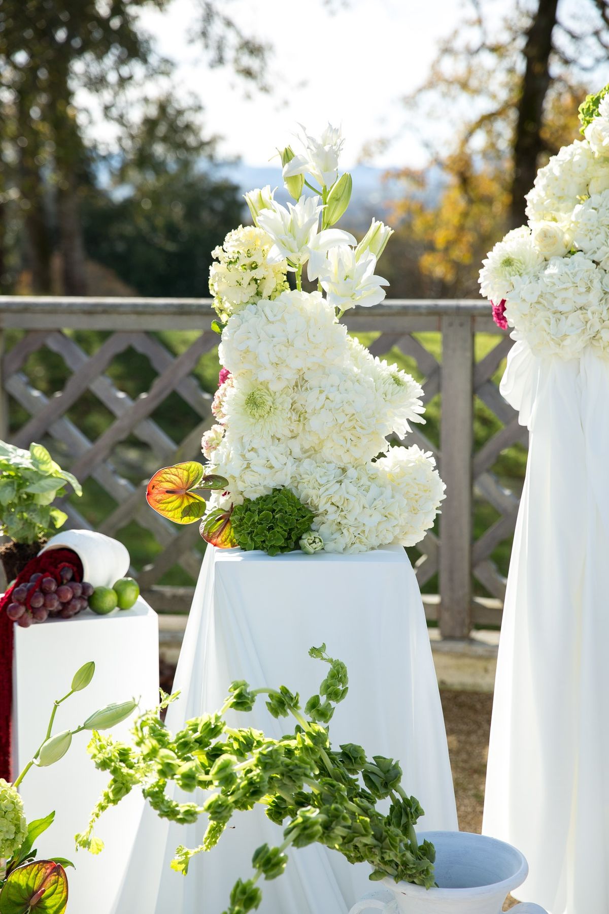 White draped ceremony pillar topped with hydrangeas, lilies and anthurium leaves