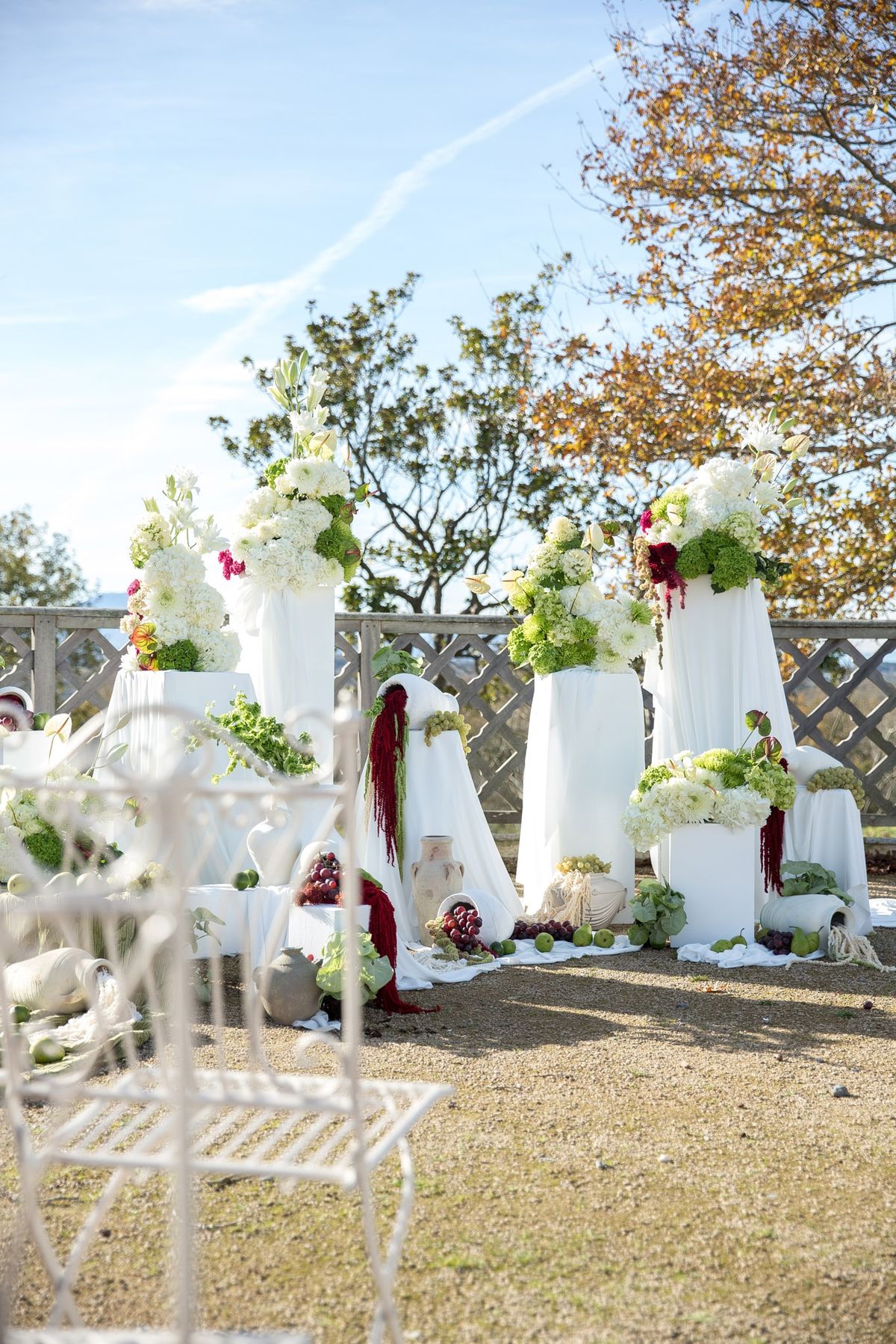 Ceremony backdrop with white draped pillars, hydrangeas and white wrought-iron chair in foreground