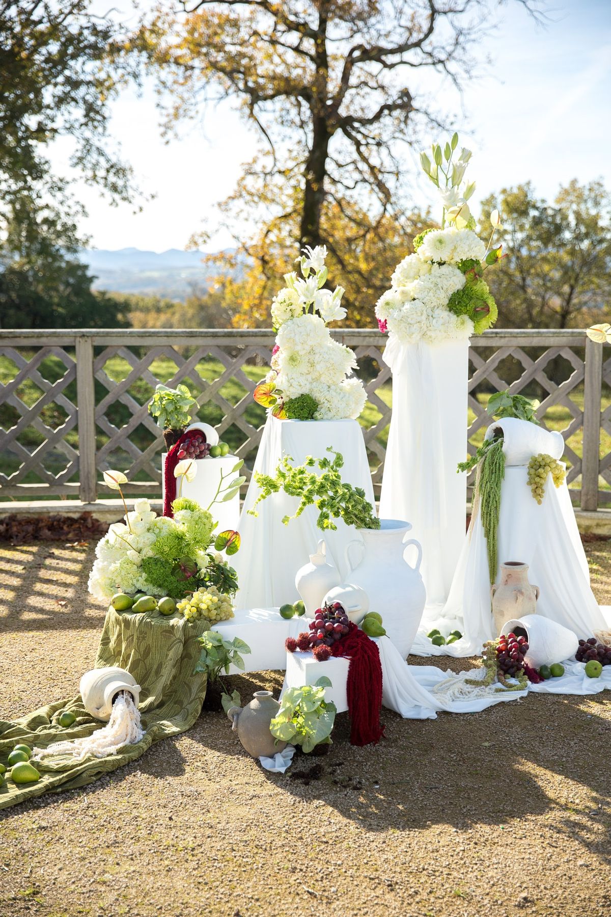 Three quarter view of ceremony backdrop with white pillars, urns, hydrangeas and green drape