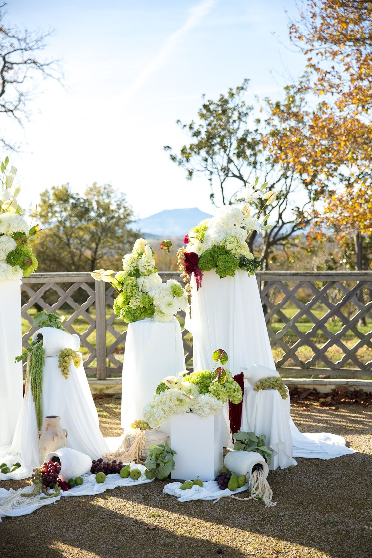 Ceremony backdrop with stacked white plinths, hydrangeas, amaranthus and lime piles at base
