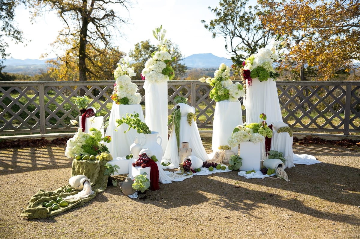 White plinths topped with hydrangeas and dark berry sprays against wood lattice fence