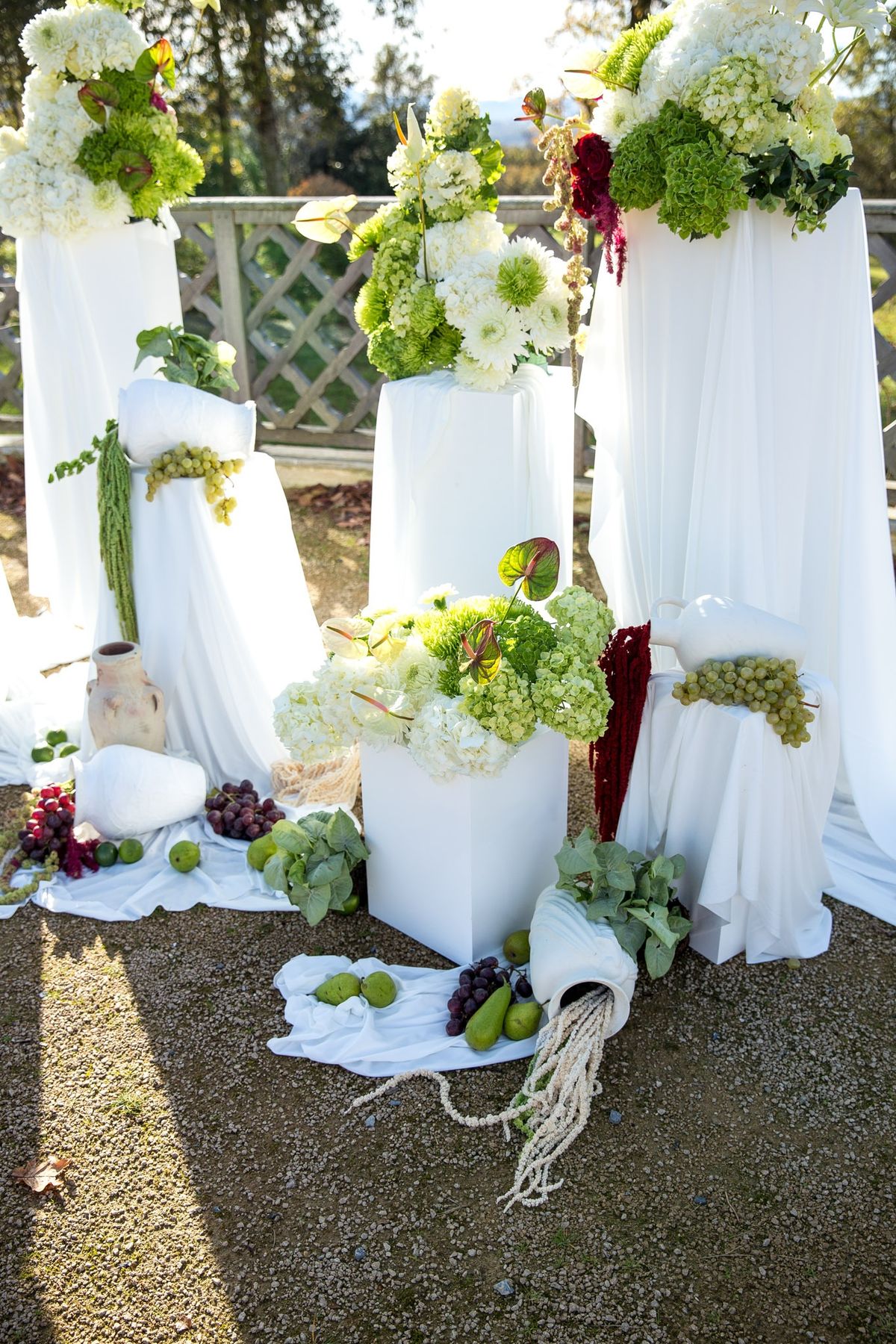 Ceremony backdrop with white draped plinths topped with hydrangeas and anthuriums