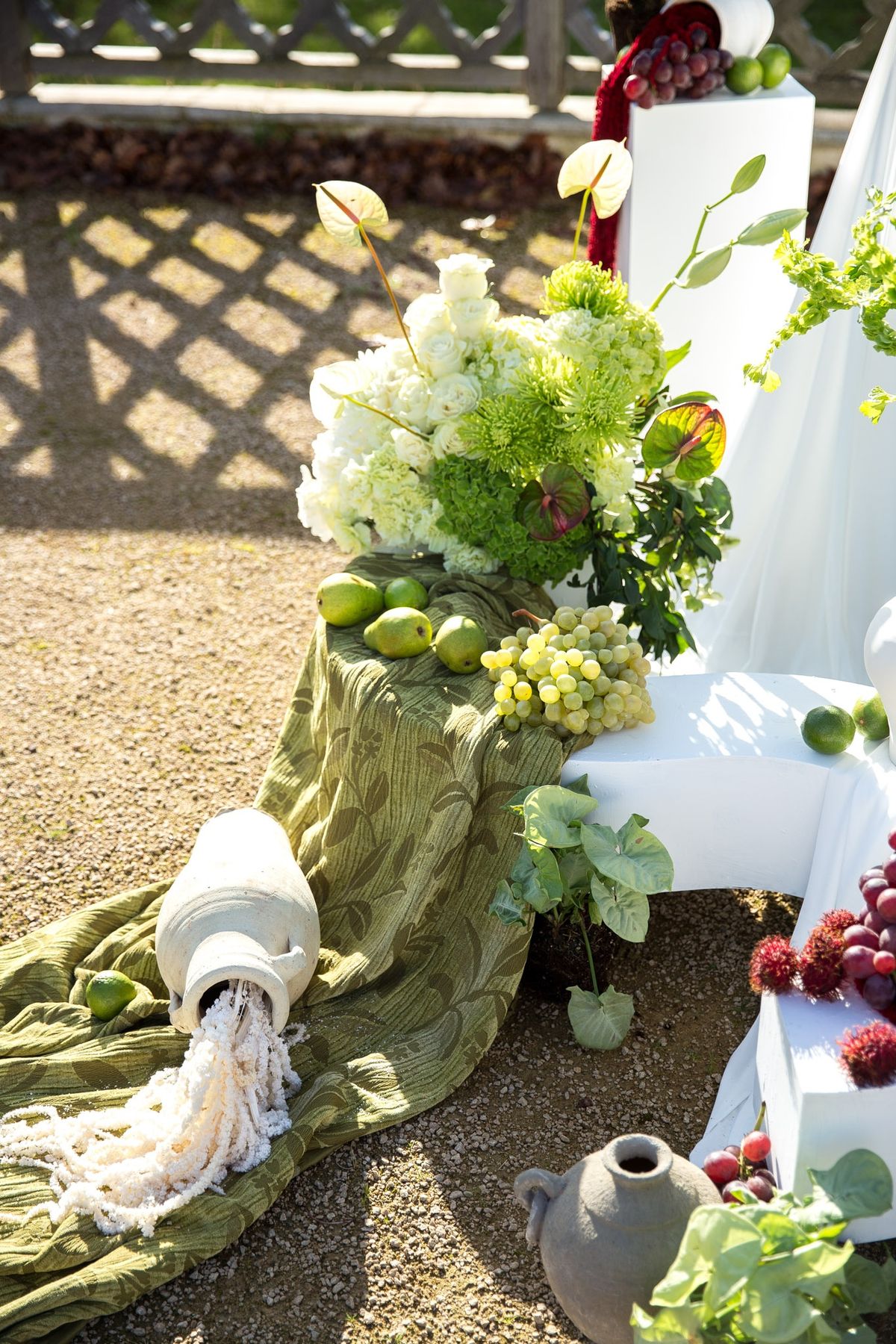Side angle of ceremony backdrop with tipped vessel spilling pears onto green textile runner