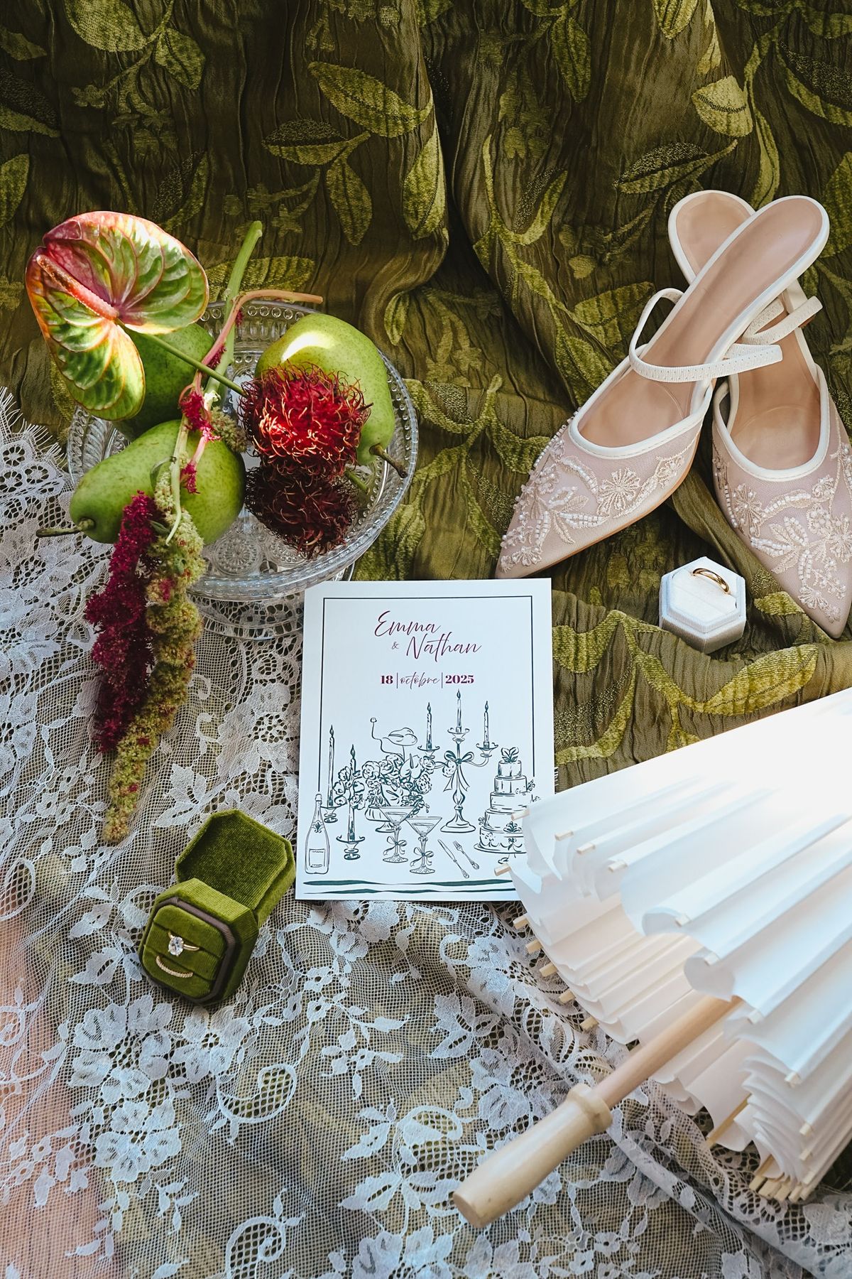 Top down stationery scene with mules, program card, green ring box with gold band, fan and fruit