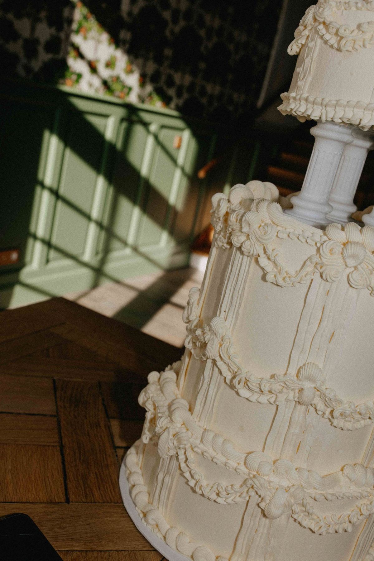 Vintage piped tiered cake on parquet floor in panelled chateau room with sage green wainscot