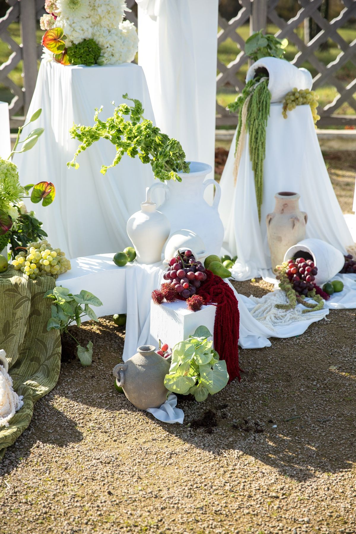Golden hour lower ceremony backdrop with green textile, white urn, grapes and warm raking light