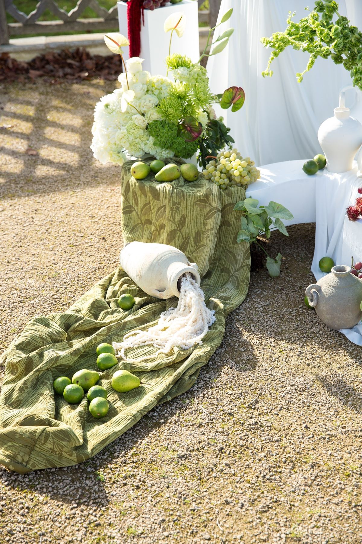 Golden hour vignette of florals spilling from ceramic vessel beside pears and limes on green cloth