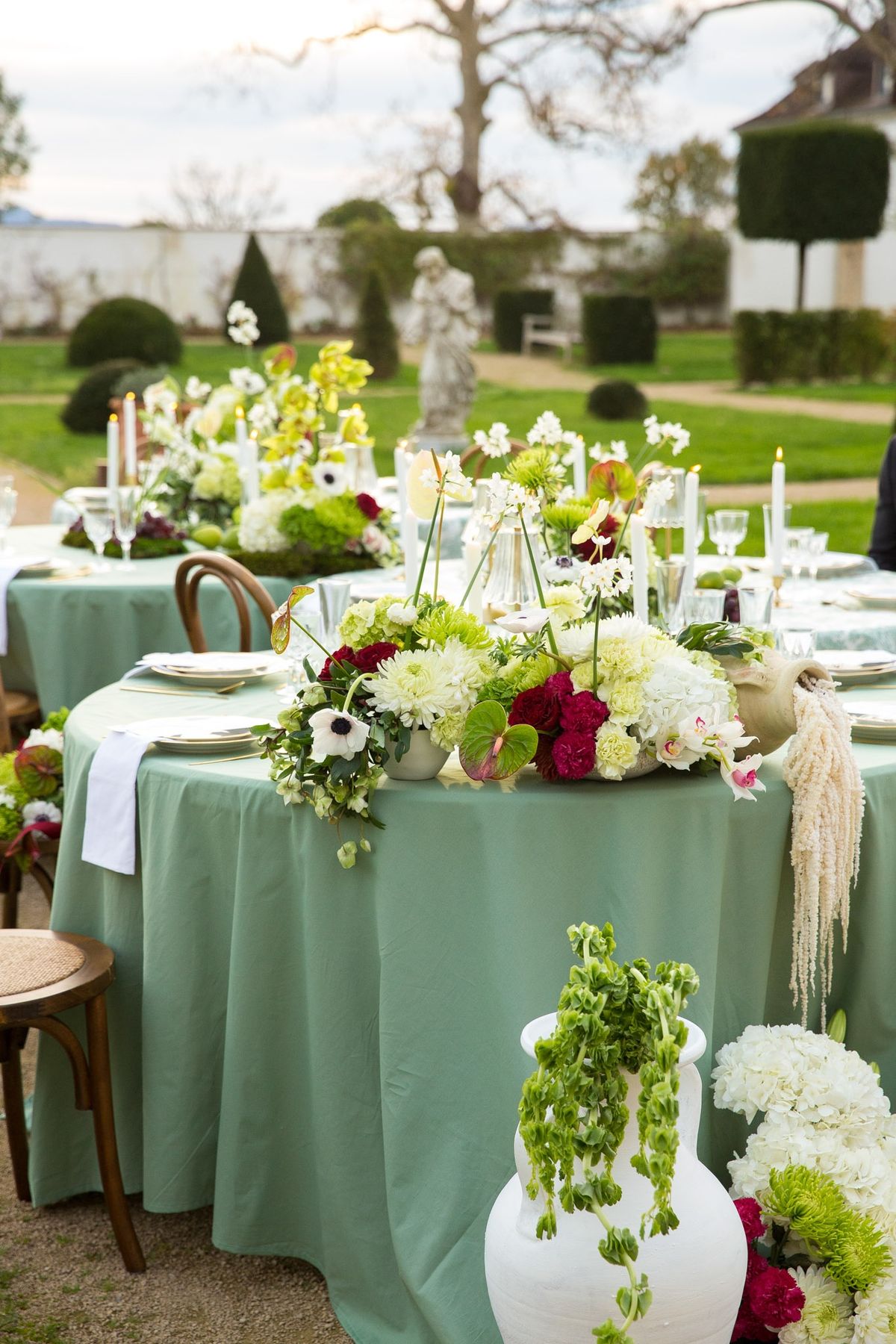 Sage round table with cascading centerpiece of hydrangeas, dahlias and anemones, statue behind
