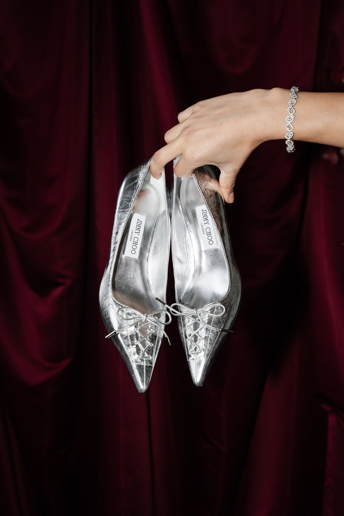 Bride holding silver Jimmy Choo shoes against red velvet at Domaine des Halles