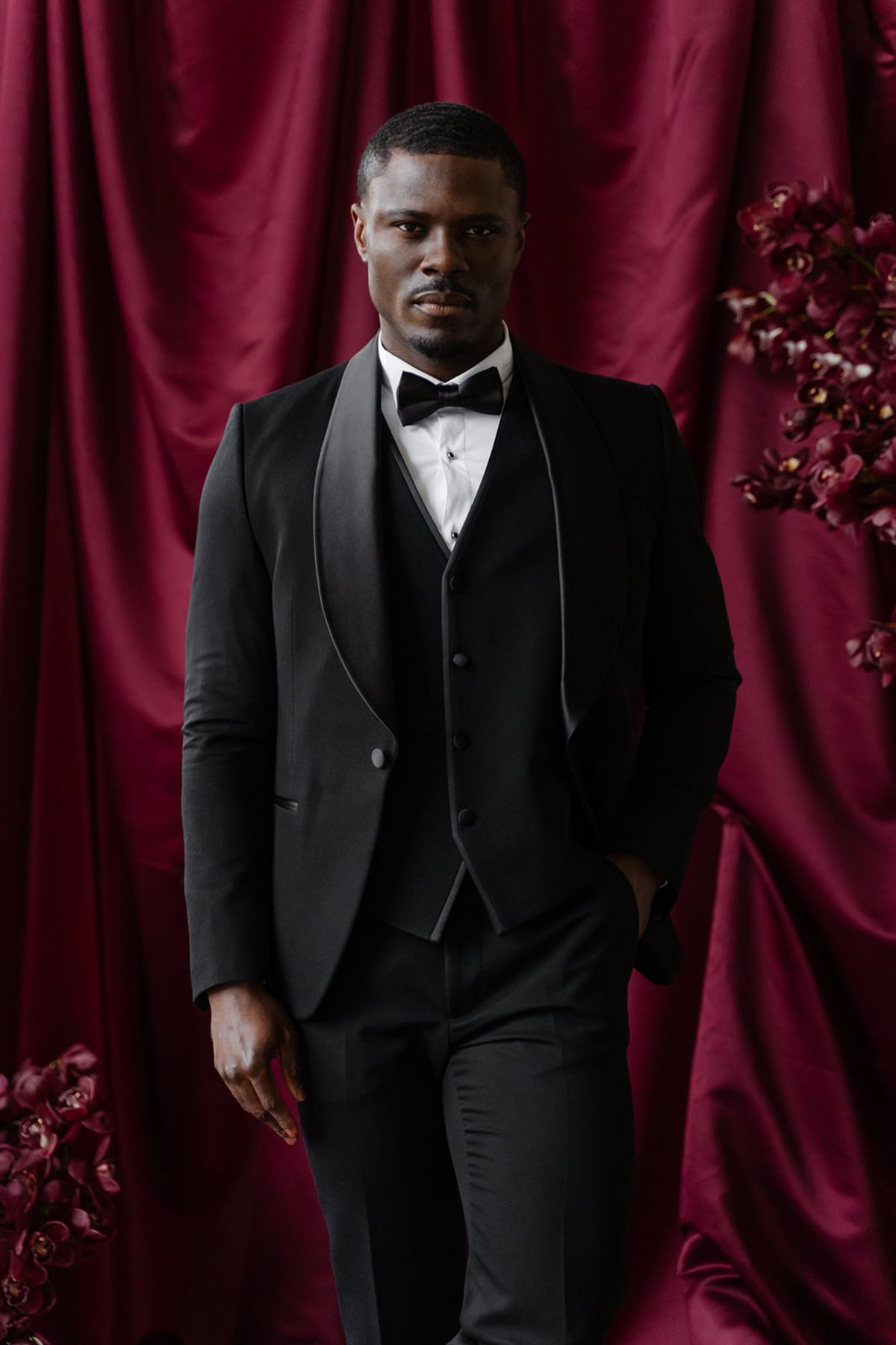 Groom portrait in black tuxedo against magenta satin backdrop at Domaine des Halles