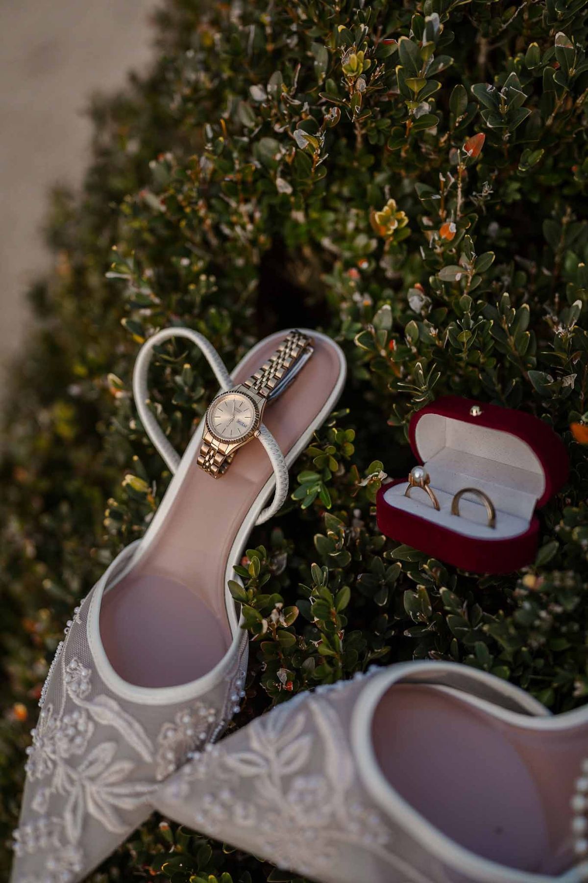 Bridal shoes, watch, and rings on boxwood hedge at Chateau d'Hazeville