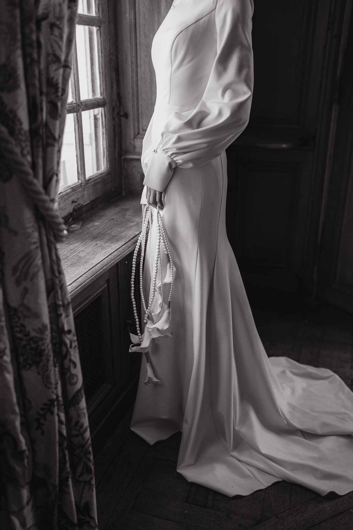 Bride in satin gown by window at Chateau d'Hazeville
