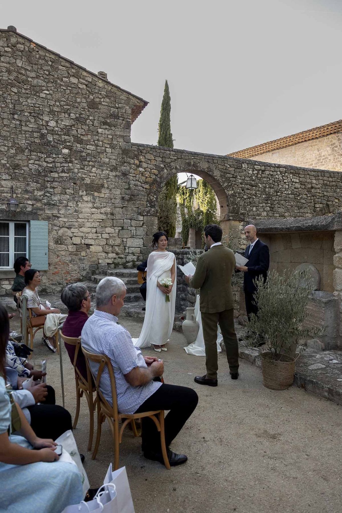 Couple facing each other exchanging vows under olive branch arch at outdoor ceremony