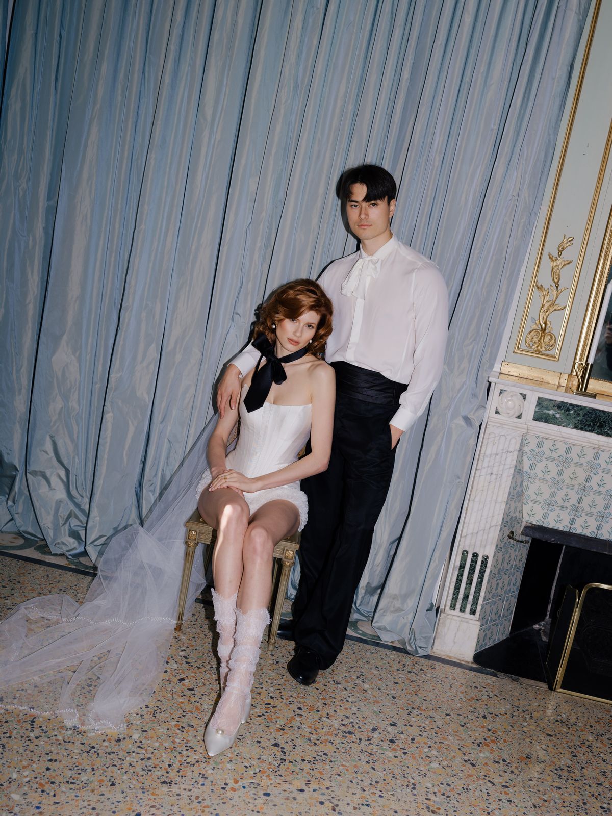 Couple poses against soft blue silk with bride in black neck ribbon and long sheer veil pooling on floor