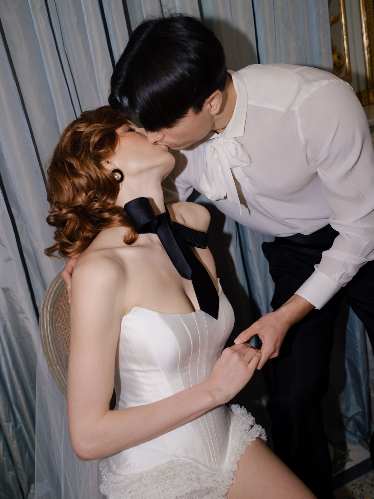 Tightly cropped couple kiss with black satin neck ribbon falling between bride and groom