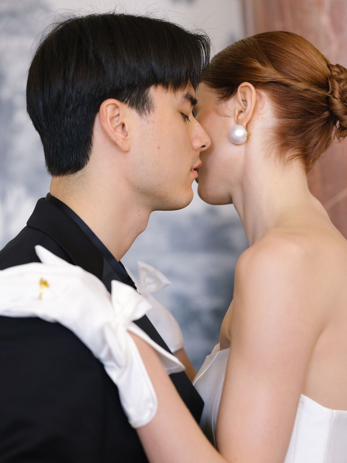 Close-up of couple kiss with groom's white glove on bride's shoulder and pearl drop earring