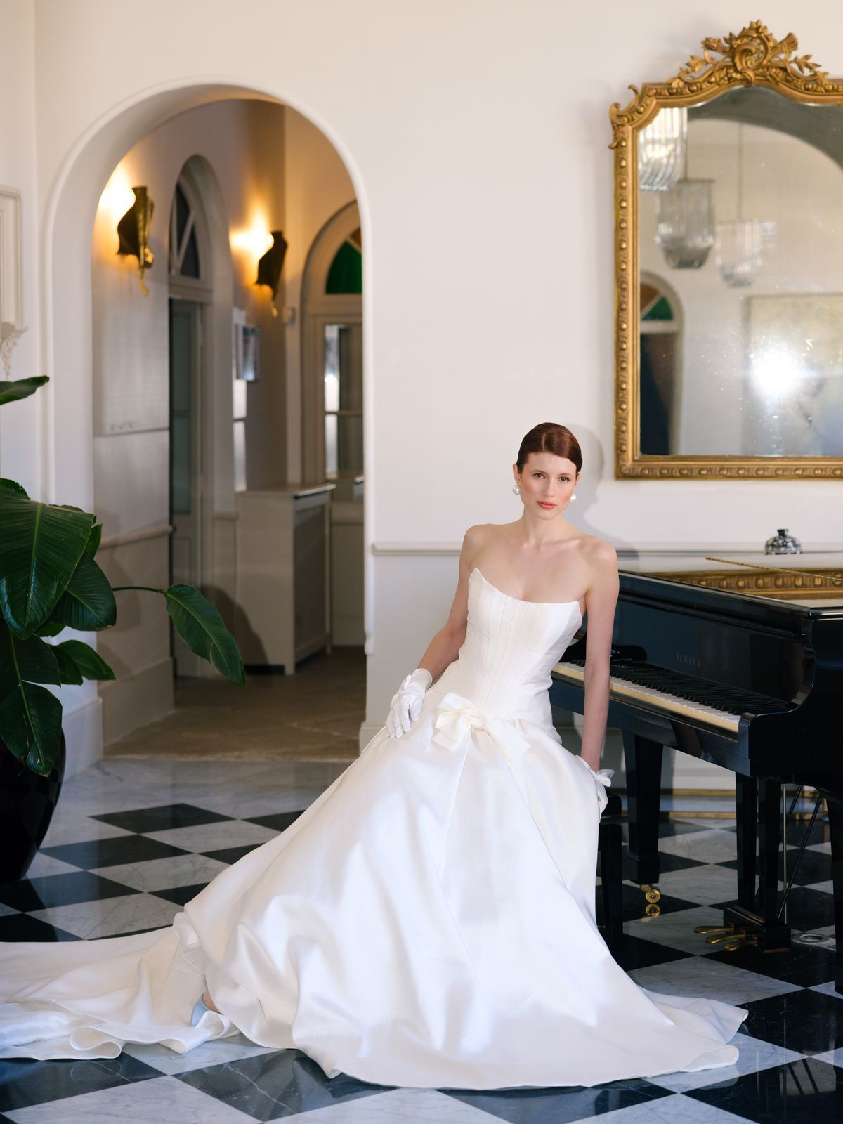 Bride beside grand piano in strapless A-line gown with bow waist on black and white marble floor