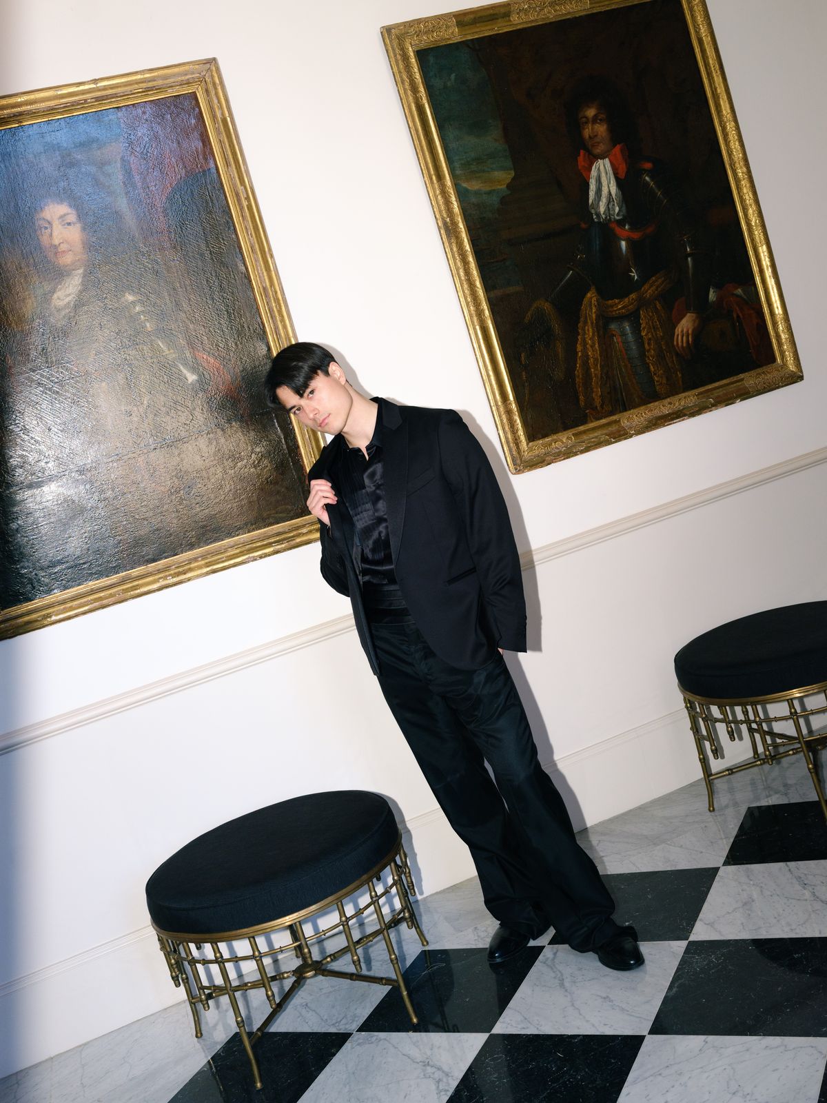 Groom tilts into pose between two gilt-framed historic portraits in marble château salon
