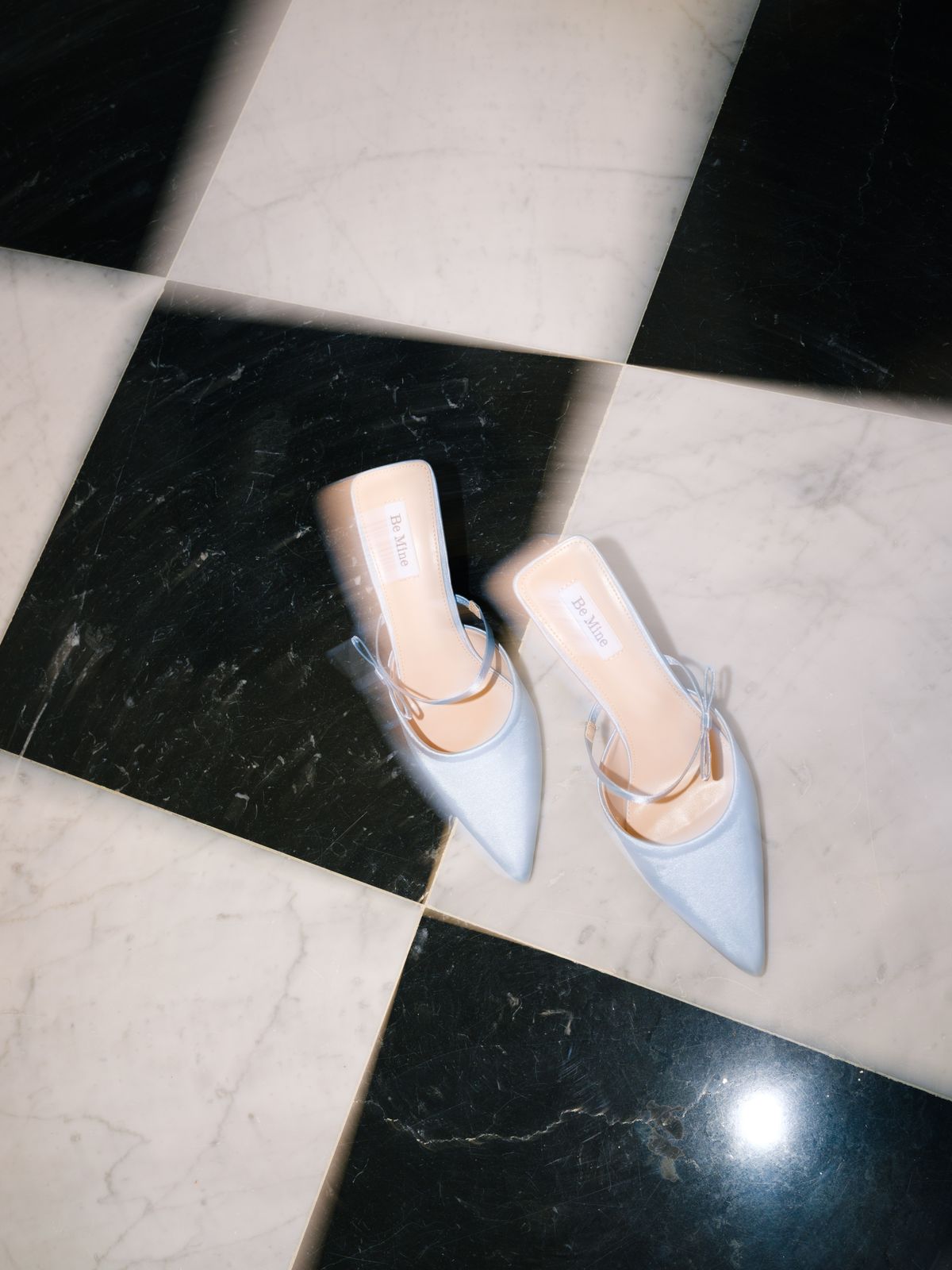 Pale blue satin pointed slingback heels arranged on black and white checkerboard marble floor