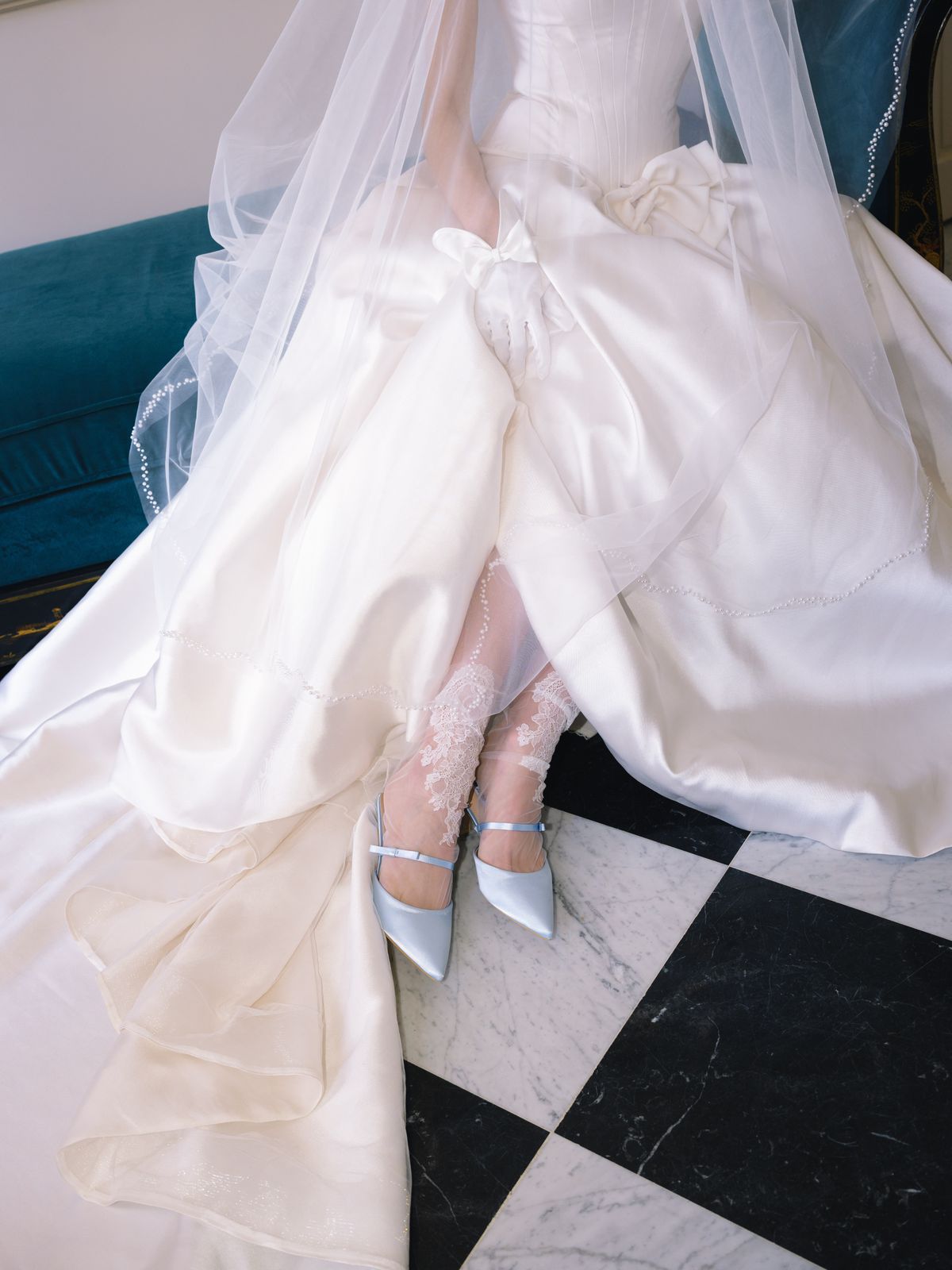Detail of bride's satin gown bow waist, lace stockings and pale blue slingbacks on marble floor