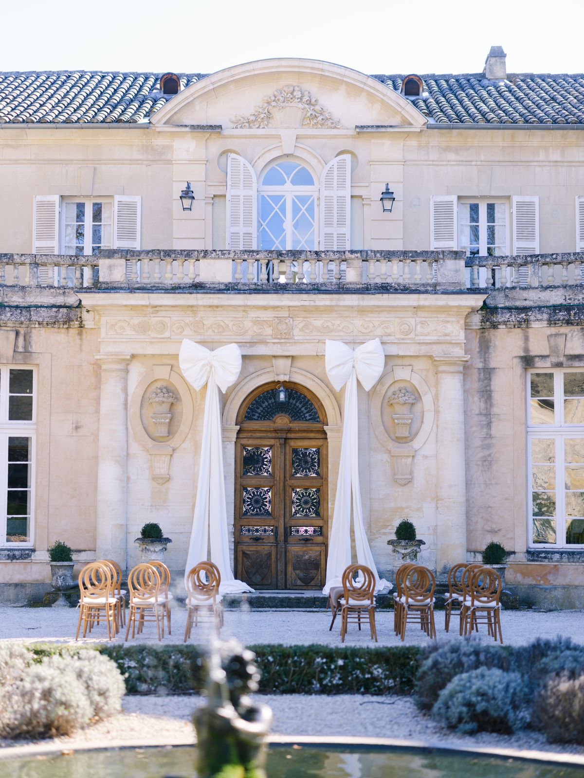 Neoclassical château facade with two oversized ivory satin bows over carved wood door and ceremony chairs