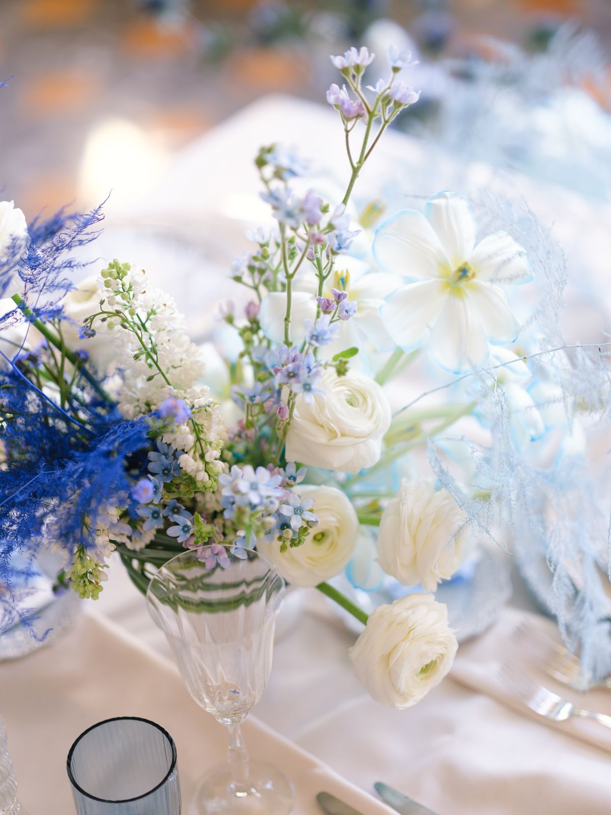 Close-up arrangement of white ranunculus, pale blue delphinium and dyed blue feathered florals in coupe